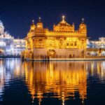 Night view of the Golden Temple in Amritsar illuminated with golden lights, reflecting beautifully in the sacred pool against a clear dark sky.